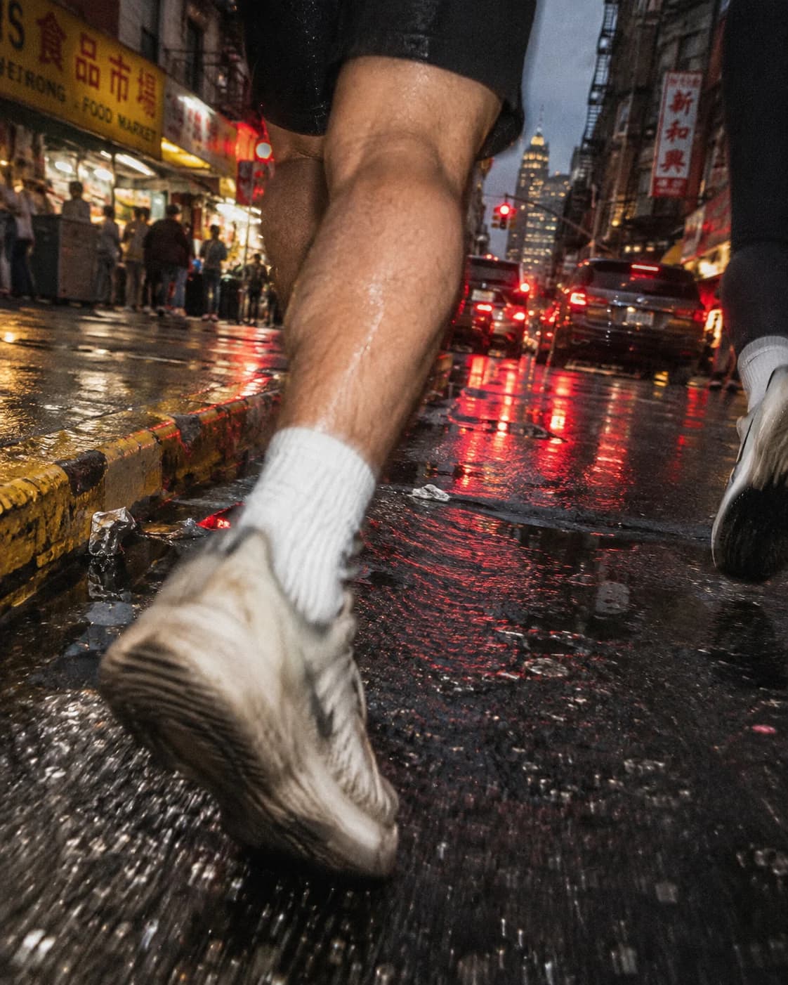 A worn running shoe blurs past wet pavement and red traffic reflections.